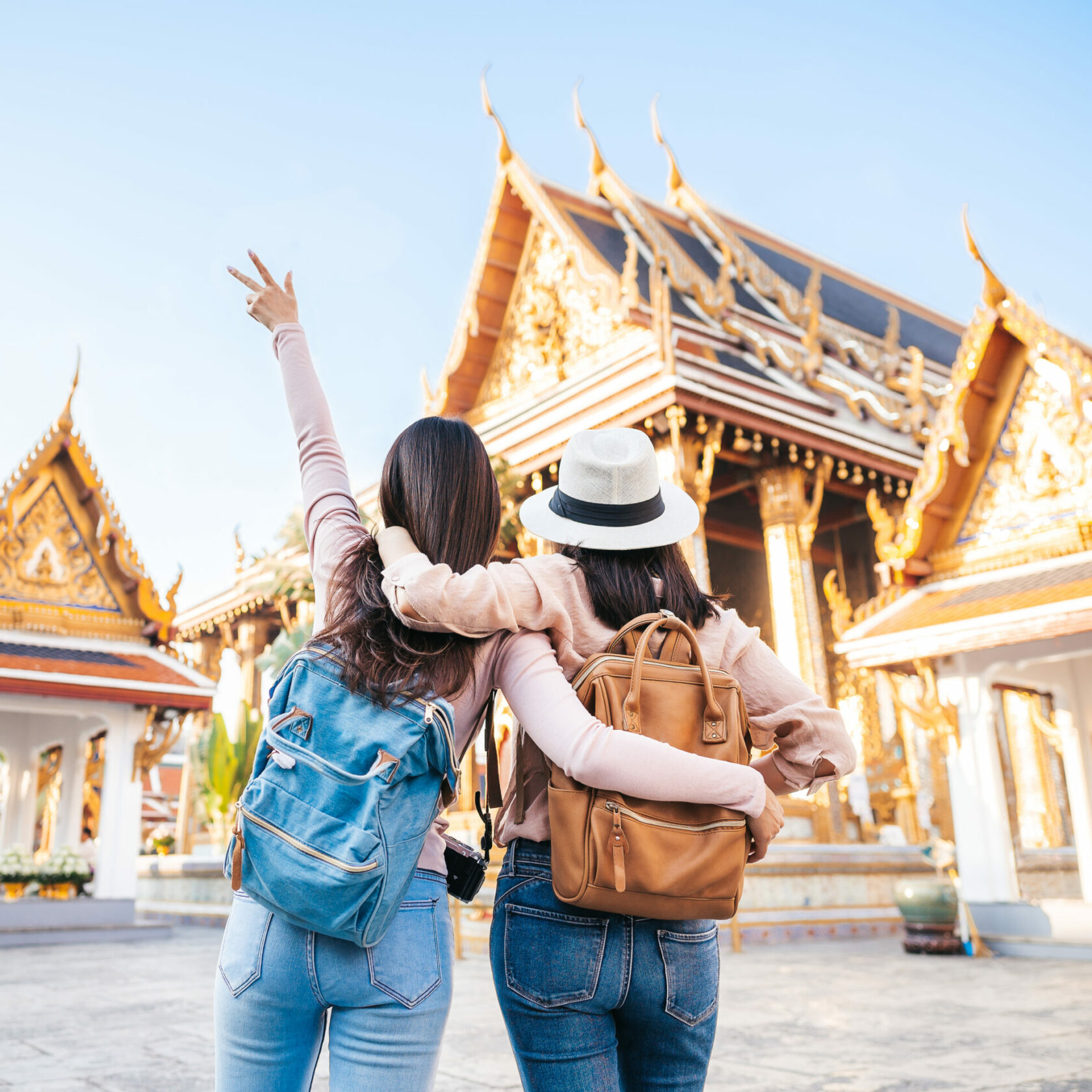 two Asian women traveller best friends having fun during vacation in temple Rear view of two Asian women traveller best friends having fun during vacation in temple of the emerald buddha in Thailand